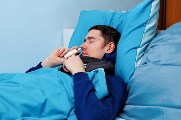 Image d'un homme malade utilisant un vaporisateur nasal en position couchée dans son lit