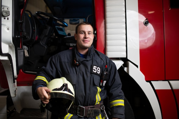 Image de l'homme pompier avec un casque à la main sur fond de camion de pompiers