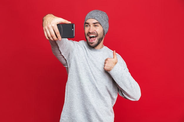 Image d'un homme de race blanche de 30 ans en tenue décontractée en riant tout en prenant selfie photo sur téléphone portable isolé