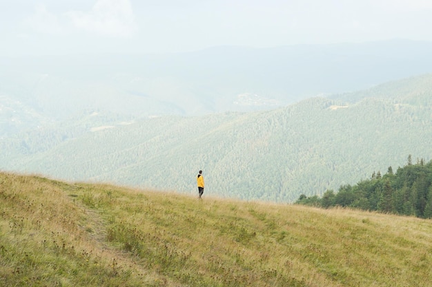 Image horizontale d'un jeune homme dans une veste jaune marchant dans un pré avec de l'herbe jaunie dans les hautes terres Le concept d'unité avec la nature repos et solitude