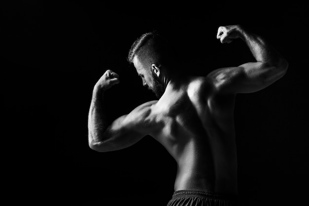 L'image incolore du dos du torse d'un body builder masculin attrayant sur fond de studio noir.