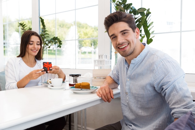 Image de l'incroyable jeune couple amoureux assis au café, manger des desserts et boire du thé. Homme regardant tandis que sa petite amie la regarde présent.