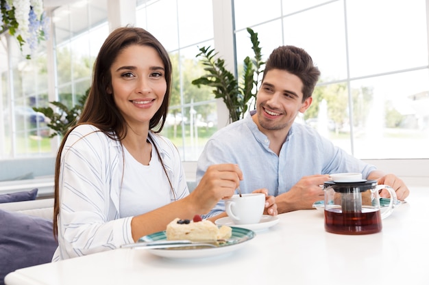 Image de l'incroyable jeune couple amoureux assis au café, manger des desserts et boire du thé.