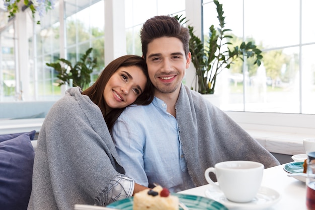 Image de l'incroyable jeune couple amoureux assis au café, manger des desserts et boire du thé.