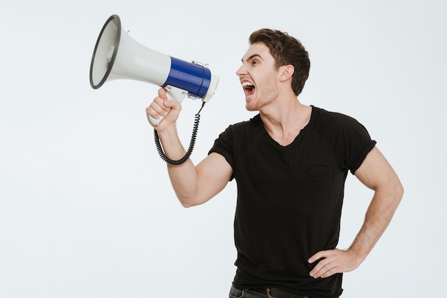 Image de jeune bel homme vêtu d'un t-shirt noir debout sur fond blanc criant avec un embout buccal.