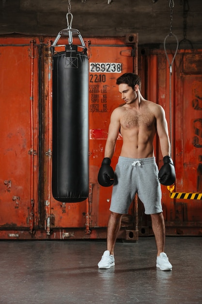 Image de jeune boxeur concentré posant dans une salle de sport avec sac de frappe.