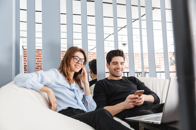 Image d'un jeune couple d'amoureux heureux à la maison à l'intérieur à l'aide d'un ordinateur portable discutant par téléphone.