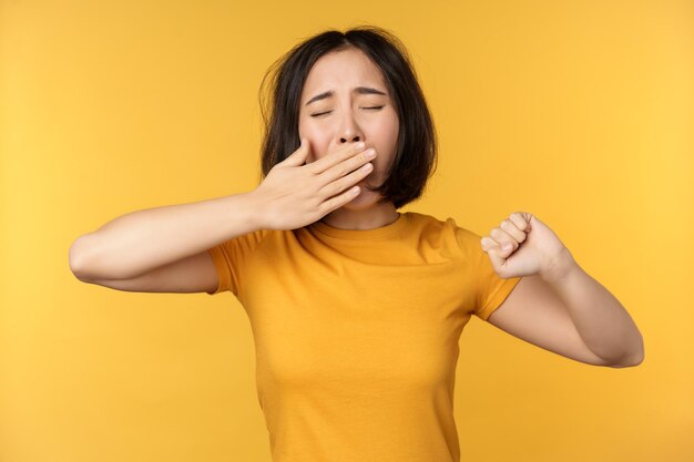 Image d'une jeune étudiante asiatique bâillant se sentant fatiguée debout somnolente sur fond jaune