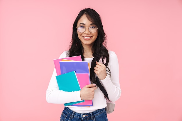 Image d'une jeune étudiante asiatique brune portant des lunettes tenant des dossiers papier isolés sur rose