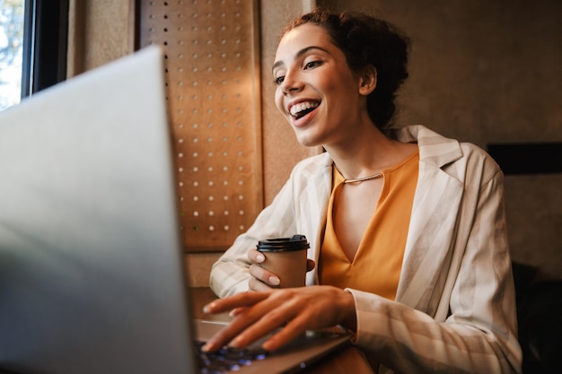 Image d'une jeune femme d'affaires heureuse à l'intérieur d'un café à l'aide d'un ordinateur portable.