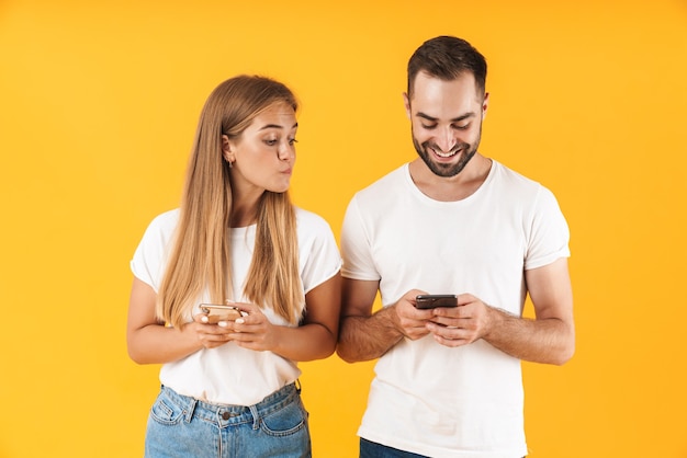 Image d'une jeune femme espionnant et regardant le téléphone portable de son petit ami isolé sur un mur jaune