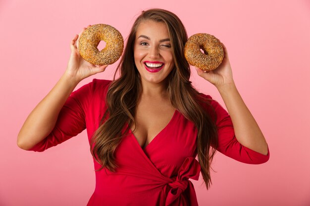 Image d'une jeune femme heureuse isolée sur mur rose tenant des beignets.