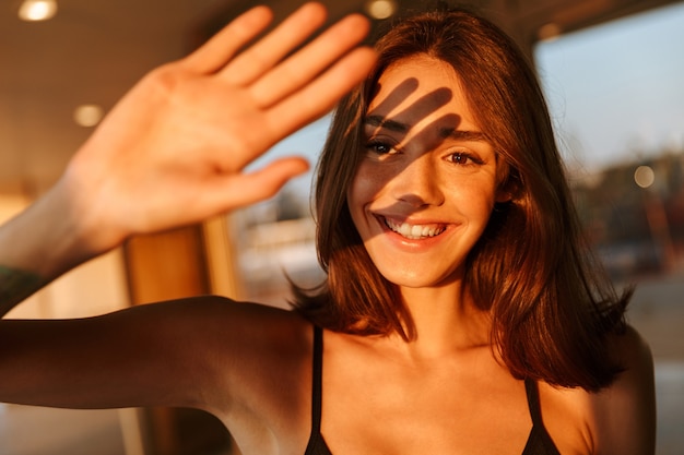 Image d'une jeune femme joyeuse en tenue de sport couvrant son visage avec la main du soleil en marchant dans la rue