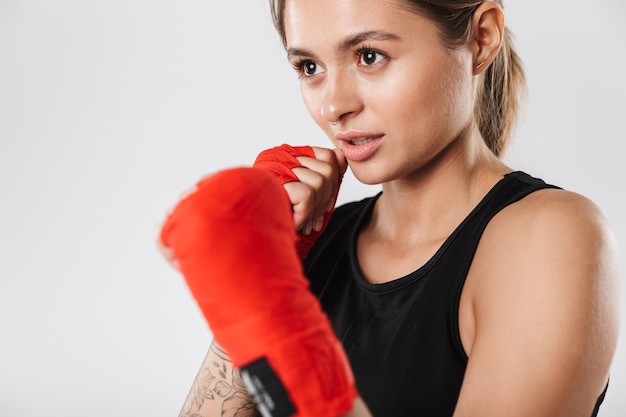 Image d'une jeune femme portant une formation de vêtements de sport dans des enveloppements de boxe isolés sur un mur blanc