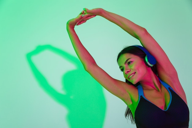 Image d'une jeune femme de remise en forme forte et joyeuse qui fait des exercices d'étirement isolés avec des lumières flash LED écoutant de la musique avec des écouteurs.