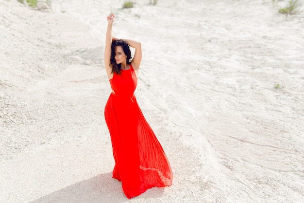 Image avec une jeune fille brune vêtue d'une robe rouge et dansant dans le désert