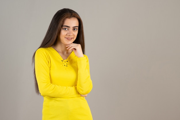 Image de jeune fille en haut jaune debout et posant sur un mur gris.