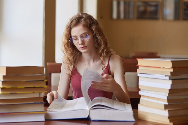 Image d'une jeune fille qui travaille dur et réfléchie en retournant des pages d'un livre énorme, à la recherche d'informations appropriées pour le projet d'étude, en faisant soigneusement le devoir à la maison.