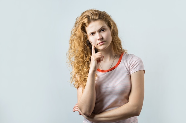 Image d'une jeune fille réfléchie. Regarder la caméra a une idée. Se dresse sur un fond blanc.