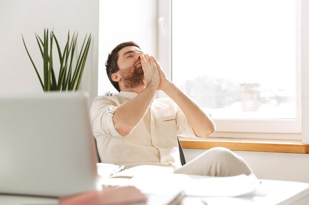 Image de jeune homme d'affaires de 30 ans portant une chemise blanche à l'aide d'un ordinateur portable, tout en travaillant dans un bureau moderne