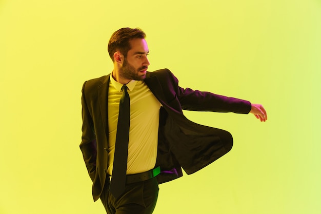 Image d'un jeune homme d'affaires sérieux en costume formel faisant des gestes en marchant isolé sur un mur jaune