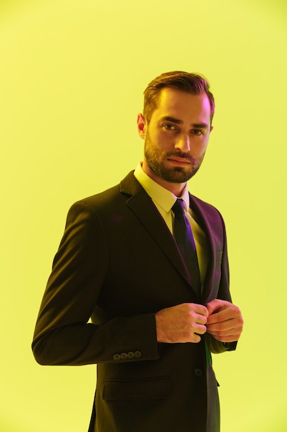 Image d'un jeune homme d'affaires sérieux en costume formel touchant sa veste isolée sur un mur jaune
