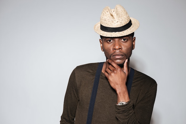 Image d'un jeune homme africain séduisant portant un chapeau debout en studio. Isolé sur fond gris.