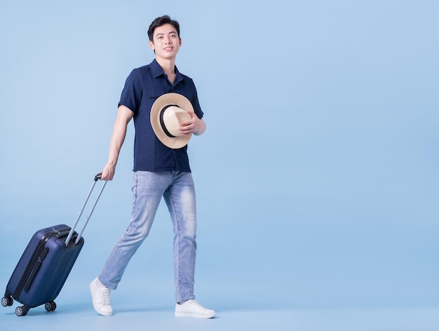 Image d'un jeune homme asiatique tenant une valise sur le concept de voyage de fond bleu