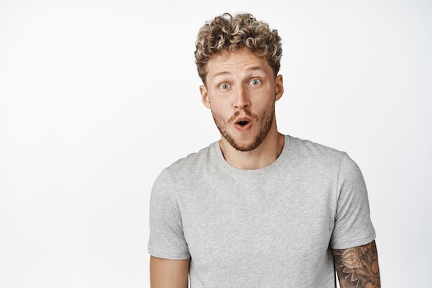 Image d'un jeune homme blond qui a l'air surpris, étonné par quelque chose de cool qui vérifie la publicité debout dans un t-shirt gris sur fond blanc