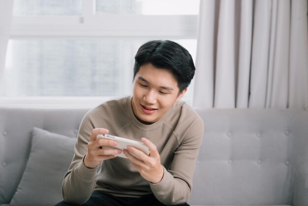 Image d'un jeune homme joyeux et souriant à l'intérieur à la maison jouer à des jeux par téléphone portable