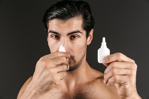 Image d'un jeune homme malade posant isolé tenant un flacon pulvérisateur nasal avec une serviette.