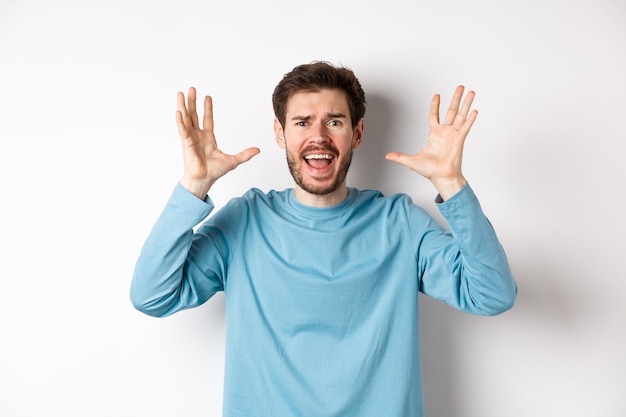 Image d'un jeune homme paniqué crier et serrer la main, crier à la caméra frustré ou inquiet, paniqué sur fond blanc