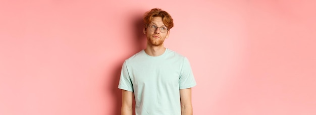 Image d'un jeune homme rousse avec une barbe portant un t-shirt et des lunettes regardant à gauche avec ennuyé sans se soucier