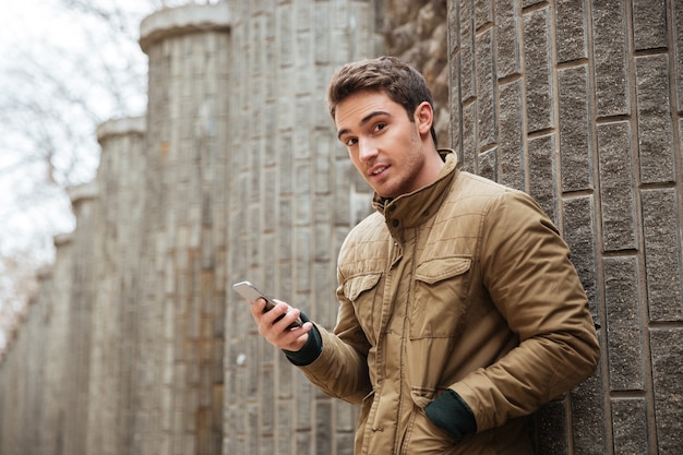 Image d'un jeune homme séduisant marchant dans la rue et discutant avec son téléphone à l'extérieur. Regardez la caméra.