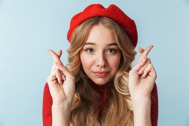 Image de jolie femme blonde des années 20 portant un béret rouge en gardant les doigts croisés en position debout, isolé