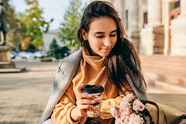 Image d'une jolie jeune femme buvant du café en déplacement dans la rue de la ville Femme joyeuse dans la rue de la ville buvant un cappuccino chaud Jolie fille brune avec une tasse de café