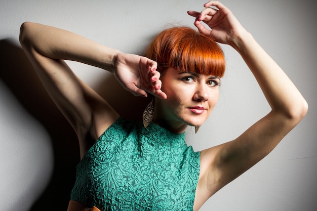 Image de jolie jeune femme rousse en robe verte debout avec les bras croisés sur fond de mur gris à la caméra