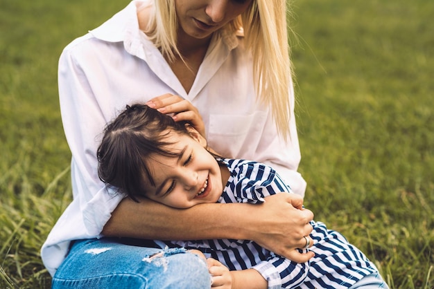 Image d'une jolie petite fille heureuse embrassant et allongée sur les jambes de sa mère en plein air Mère et fille aimantes assises sur l'herbe verte dans le parc Maman et enfant se câlinant s'amusant à l'extérieur Bonne relation