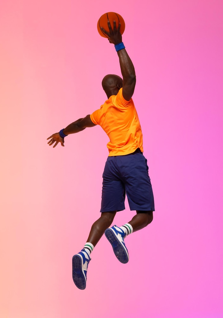 Photo image d'un joueur de basket-ball afro-américain sautant avec du basket-ball sur fond rose à orange. concept de sport et de compétition.