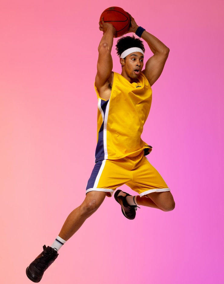 Photo image d'un joueur de basket-ball biracial sautant en l'air avec du basket-ball sur fond rose. concept de sport et de compétition.