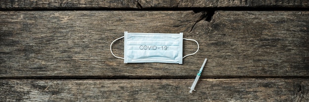 Image large d'un masque de protection médical avec le signe Covid 19 et une injection placée sur un fond en bois rustique.