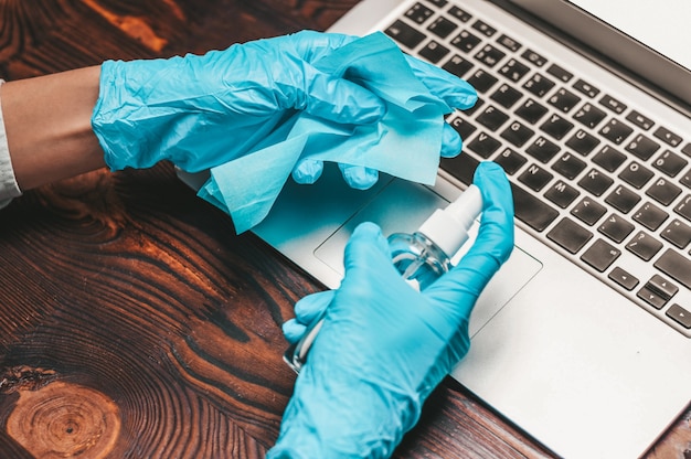 Image de mains dans des gants bleus avec microfibre et agent de nettoyage. Concept de prévention pour ordinateur portable. Technique mixte