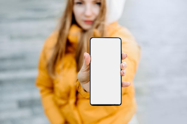 Image de maquette d'une belle étudiante montrant un téléphone portable avec un écran blanc vierge assis dans la rue