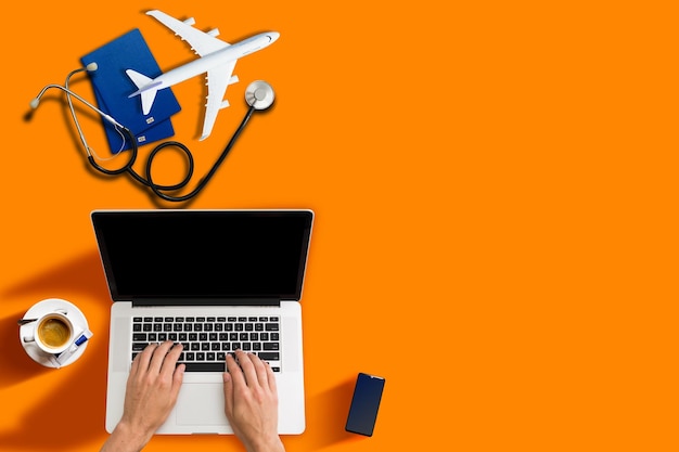 Image maquette du stéthoscope médical, passeport, ordinateur portable, avion isolé sur fond orange. Concept de voyage, de voyage et d'assurance.