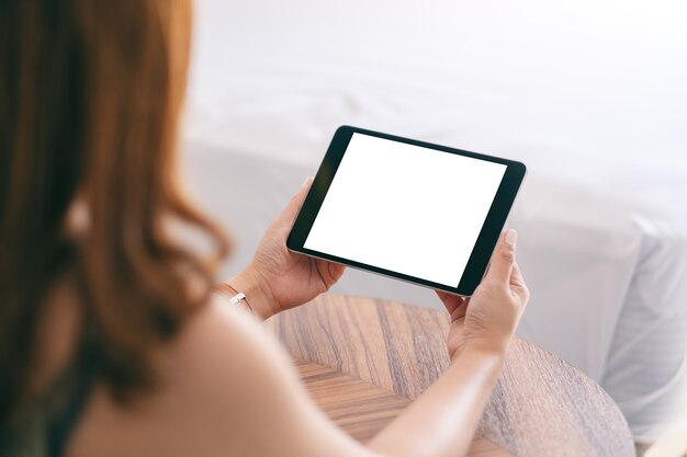 Image de maquette d'une femme tenant et à l'aide de tablet pc avec écran vide alors qu'il était assis à côté du lit