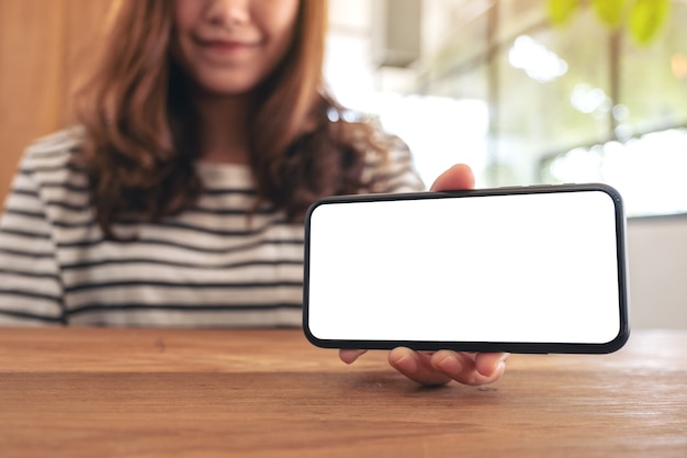 Image de maquette d'une femme tenant et montrant un téléphone mobile blanc avec écran blanc horizontalement sur table en bois