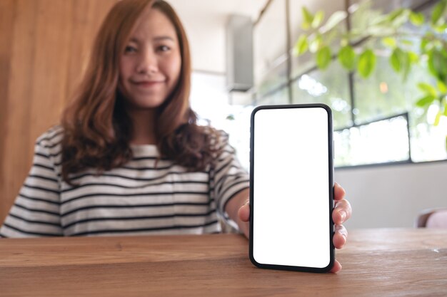 Image de maquette d'une femme tenant et montrant un téléphone mobile blanc avec écran blanc sur table en bois