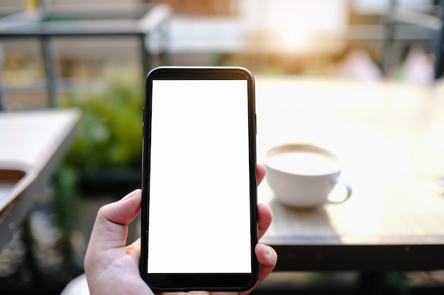 Image maquette d'une femme tenant et montrant un téléphone mobile noir avec écran blanc au café.