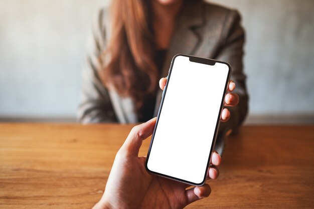 Image maquette d'une femme tenant et montrant un téléphone portable blanc avec un écran de bureau noir vierge à quelqu'un