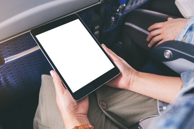 Image de maquette d'une femme tenant et regardant le tablet pc noir avec écran de bureau blanc vierge alors qu'il était assis dans la cabine